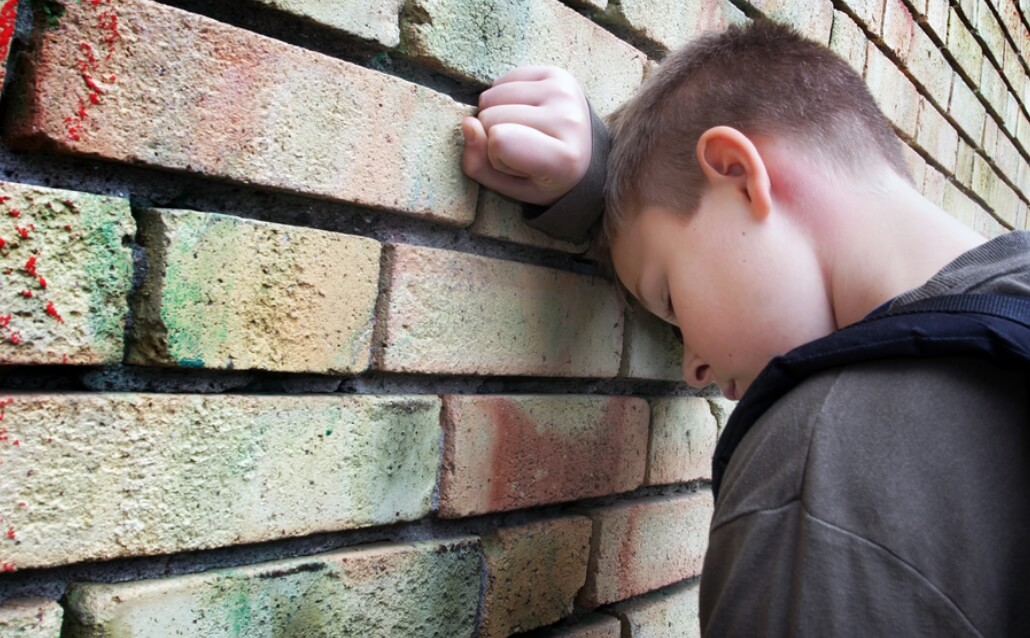 A boy looking sad, leaning with his head against the wall